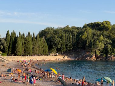 Kumsal, deniz kenarındaki turistler yeşil ağaçlarla kaplı kayalık bir tepenin yanında. Yüksek kalite fotoğraf