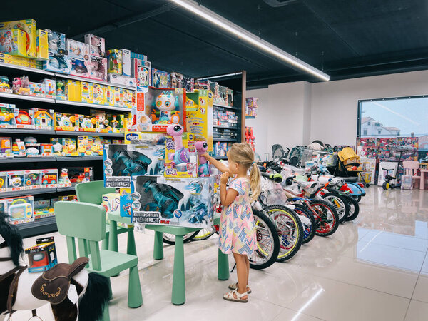 Little girl is watching toy dinosaurs in the supermarket. Side view. High quality photo