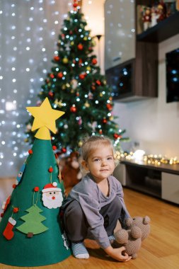 Küçük kız oyuncak bir Noel ağacının yanında oyuncak ayıyla çömeliyor. Yüksek kalite fotoğraf