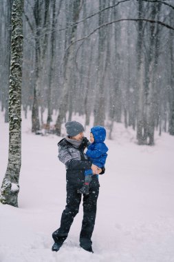 Kollarında küçük bir kızla gülümseyen anne ormanda kar altında duruyor. Yüksek kalite fotoğraf