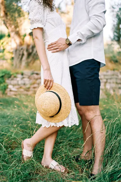 Man hugs woman by the waist standing with a straw hat in her hand in the garden. Cropped. Faceless. High quality photo