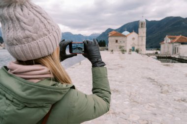 Genç bir kadın akıllı telefonuyla Meryem Ana 'nın Kayalıklardaki Kilisesi' nin fotoğrafını çekiyor. Arkadan bak. Karadağ. Yüksek kalite fotoğraf