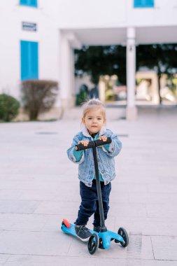 Küçük kız bahçede bir scooterla dudağını ısırıyor. Yüksek kalite fotoğraf