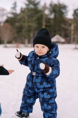 Küçük çocuk karda yürür, ellerini önündeki eldivenlerle tutar. Yüksek kalite fotoğraf