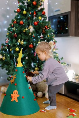 Küçük kız süslü bir Noel ağacının yanındaki keçeli ağaca oyuncak asıyor. Yüksek kalite fotoğraf