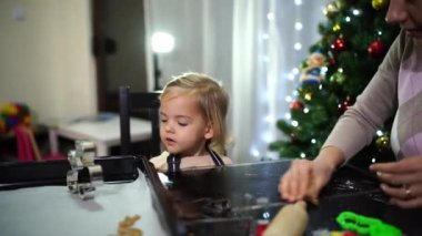 Annesi hamur kırıntılarını toplarken küçük kız elinde bir kurabiye bıçağı tutuyor. Yüksek kalite 4k görüntü
