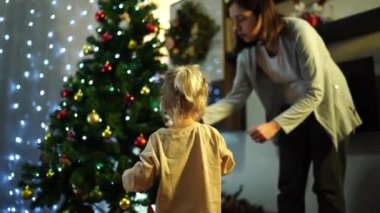 Annesiyle küçük bir kız süslü bir Noel ağacında oyuncakları düzeltiyor. Yüksek kalite 4k görüntü