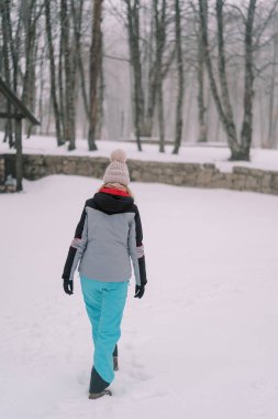 Genç bir kadın karla kaplı bir ormanda yürüyor, ayaklarına bakıyor. Arkadan bak. Yüksek kalite fotoğraf