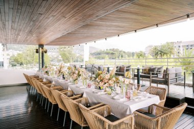 Long festive table on the restaurant terrace with panoramic views of the green park and houses. High quality photo clipart