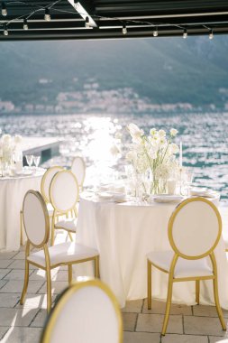 Beyaz sandalyeler, rıhtımdaki bir örtünün altında elinde çiçek buketleriyle şenlik masalarının etrafında duruyorlar. Yüksek kalite fotoğraf