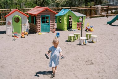 Küçük kız elinde sandaletlerle parkta kumların üzerinde yalınayak yürüyor. Yüksek kalite fotoğraf