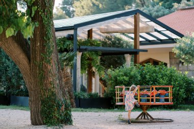 Küçük kız oyun parkında bir atlıkarıncaya tırmanır. Arkadan bak. Yüksek kalite fotoğraf