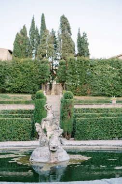 Büyük bir balığın üzerinde duran bir periyle yeşil bir bahçede antik taş çeşme. Yüksek kalite fotoğraf