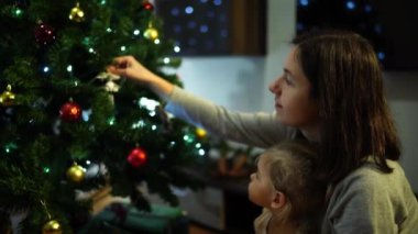 Anne kollarında küçük bir kızla bir Noel ağacına çan asıyor. Yüksek kalite 4k görüntü