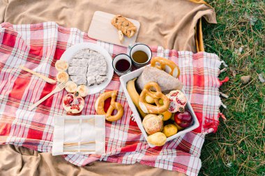 Çörekler, sepetteki meyveler ve dilimlenmiş turtanın yanında, battaniyenin üzerinde duran fincanlar. Yüksek kalite fotoğraf