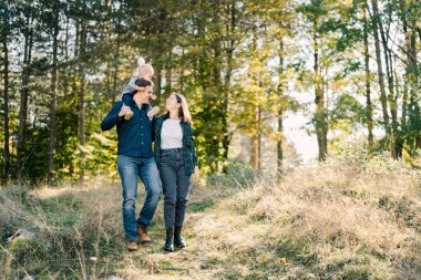 Omuzlarında küçük bir kızla babası ormanın kıyısında annemin yanında yürüyor. Yüksek kalite fotoğraf