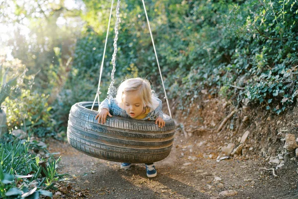 Little girl swings on a tire swing, leaning on her belly. High quality photo
