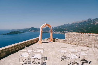 Denizin üstündeki gözlem güvertesinde düğün kemerinin önünde beyaz sandalyeler var. Yüksek kalite fotoğraf