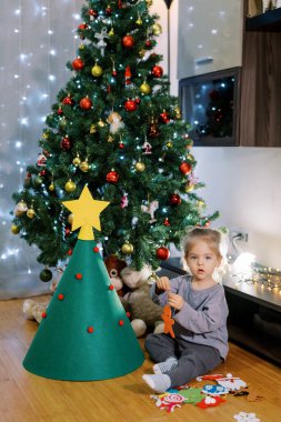 Küçük kız oyuncak bir Noel ağacının yanında yerde otururken elinde keçeli bir oyuncak tutuyor. Yüksek kalite fotoğraf