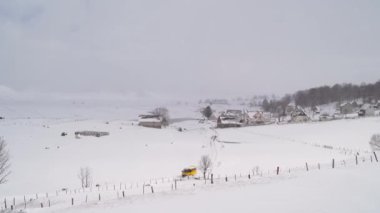 Sarı araba bir dağ köyünde karlı bir yol boyunca sürer. Yüksek kalite 4k görüntü
