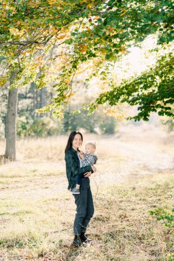 Gülümseyen anne, kollarında küçük bir kızla bir ağacın yanında duruyor. Yüksek kalite fotoğraf