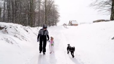 Köpek, anne ve kızının yanına koşar ve ormanın yakınındaki karlı bir yolda yürür. Yüksek kalite 4k görüntü