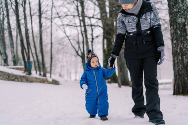 Gülümseyen anne ve küçük kız el ele tutuşarak karlı ormanda yürüyorlar. Yüksek kalite fotoğraf