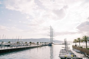 Yelkenleri açık yelkenli bir yat, dağların arka planında lüks bir marinanın iskelesinde duruyor. Yüksek kalite fotoğraf