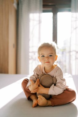 Küçük kız yatakta otururken oyuncak ayıya sarılıyor. Yüksek kalite fotoğraf