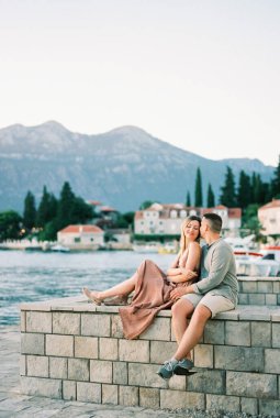 Adam, deniz kıyısındaki bir rıhtımda taş bir çitte onunla otururken tapınakta kadını öpüyor. Yüksek kalite fotoğraf