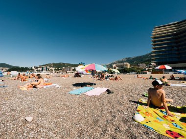 Turistler, dağların eteğindeki otellerin yanındaki plajda havlularla güneşleniyorlar. Yüksek kalite fotoğraf