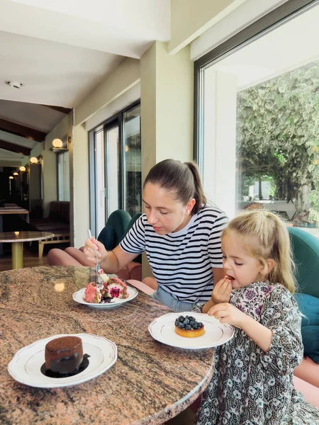 Mom with a little girl eat cakes at a table in a cafe. High quality photo