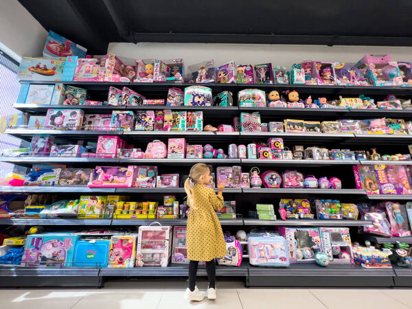 Little girl examines colorful dolls on the supermarket shelves. High quality photo