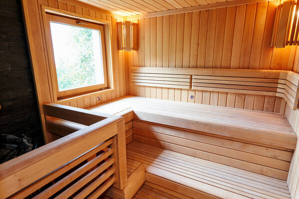 Wooden benches in the sauna with lamps in the corners near the window opposite the stove. High quality photo