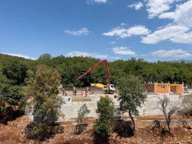 Beton pompa, yeşil ağaçların arasındaki bir inşaat sahasının temelini oluşturuyor. Yüksek kalite fotoğraf