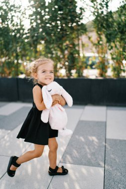 Küçük gülümseyen kız bahçede oyuncak tavşana sarılarak dolaşıyor. Yüksek kalite fotoğraf