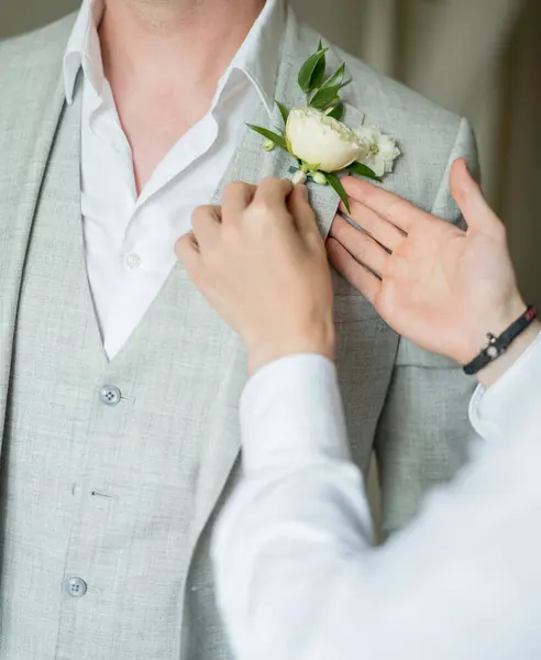 Best man attaches the boutonniere to the lapel of groom jacket. Cropped. Faceless. High quality photo