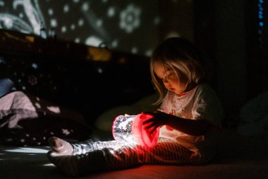 Küçük kız yatağın üzerinde oturan gece lambası projektörüne bakıyor. Yüksek kalite fotoğraf