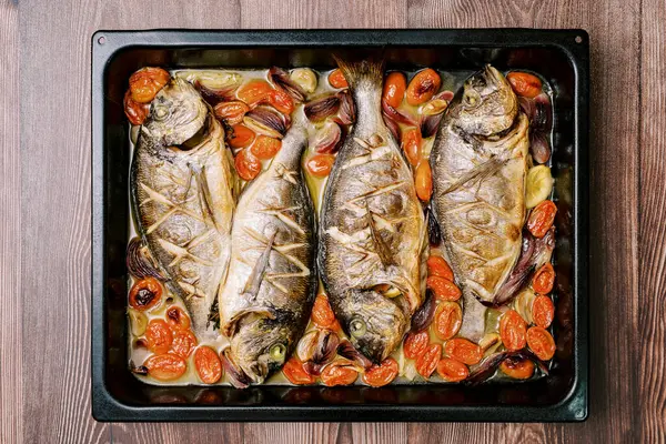Baked sea bream with vegetables on a baking sheet stands on a wooden table. Top view. High quality photo