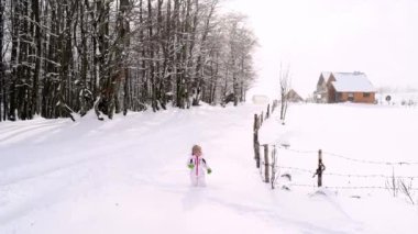 Küçük kız bir köy yolunda dizlerine kadar kar yığınlarında yürüyor. Yüksek kalite 4k görüntü