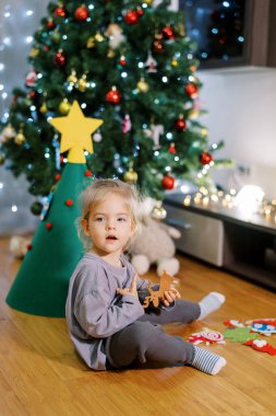 Küçük kız yerde oyuncak bir Noel ağacının yanında geyik oyuncağıyla oturuyor. Yüksek kalite fotoğraf
