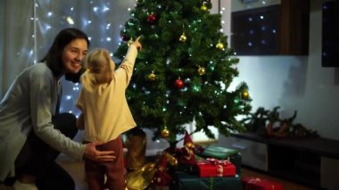 Annesiyle küçük bir kız Noel ağacını oyuncaklarla süslüyor. Yüksek kalite 4k görüntü
