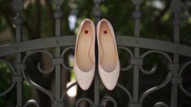 Hogl marka pembe gelinlik ayakkabıları bahçedeki işlenmiş demir bir çite asılıyor. Yüksek kaliteli FullHD görüntüler