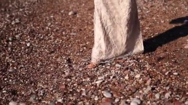 Bride in high heels walks along a pebbly beach. Close-up. High quality FullHD footage