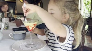 Küçük kız masada elinde bardaktan kaşıkla dondurma yiyor. Yüksek kalite 4k görüntü