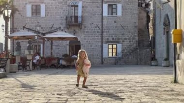 Ellerinde yumuşak bir oyuncak olan küçük bir kız eski bir kasabanın kaldırım taşları boyunca koşuyor. Yüksek kalite 4k görüntü