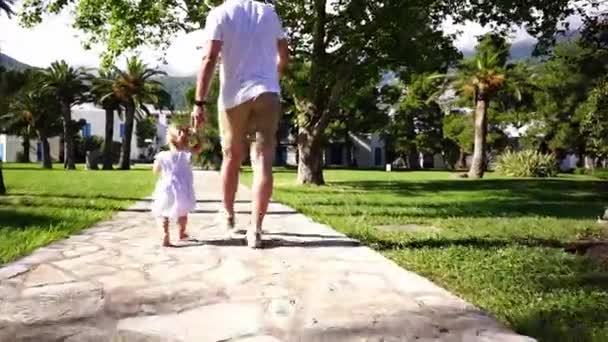 公園の道を歩いている小さな女の子とお父さん 手をつないで 高品質のフルHd映像 — ストック動画