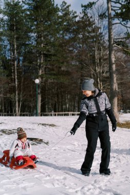Annem küçük bir kızı karlı bir ormanda kızakla taşıdı ve arkasına baktı. Yüksek kalite fotoğraf