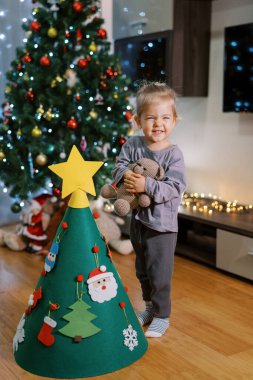 Küçük gülen kız elinde oyuncak bir ayıyla Noel ağacının yanında duruyor. Yüksek kalite fotoğraf