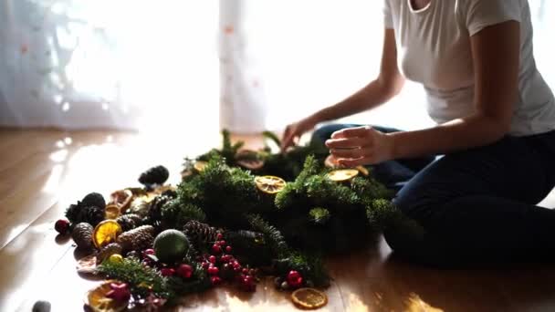 여자는 바닥에 앉아있는 가지와 오렌지 조각으로 크리스마스 화환을 장식합니다 고품질 — 비디오
